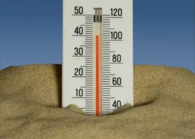 A thermometer in the sand with a blue sky in the background